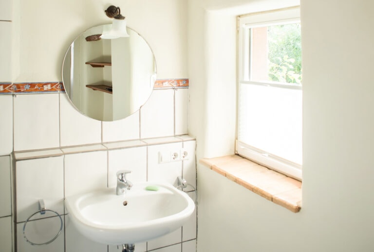 Heller, freundlicher Waschraum mit Fenster, Spiegel, Waschbecken und Handtuchhalter.